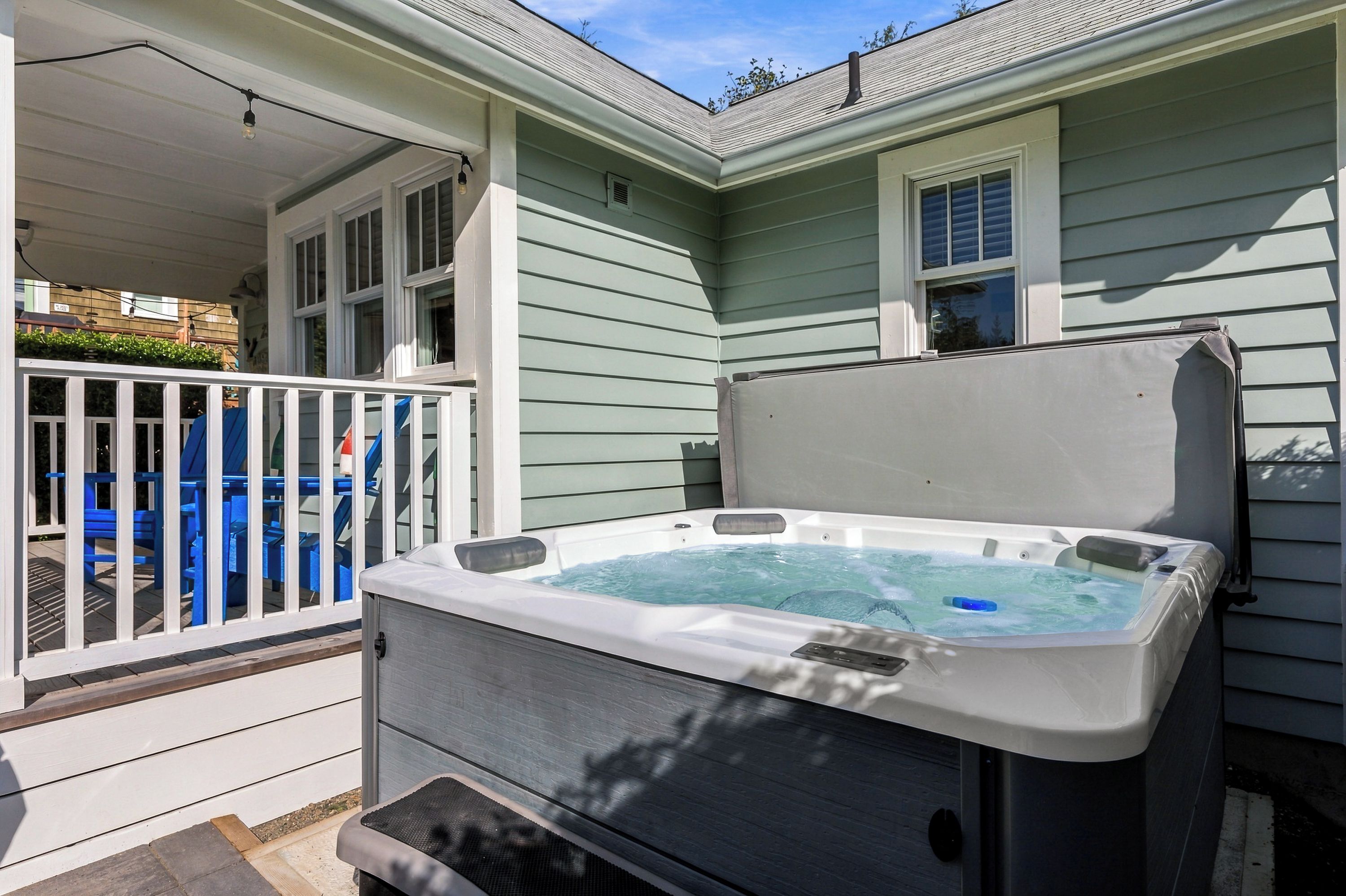 A hot tub with a cover, a white porch with a railing, and a blue outdoor seating area.