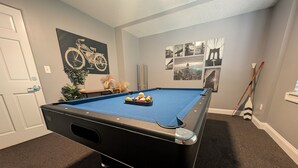 Een biljart in een kamer met een deur, een potplant en wanddecoratie.
