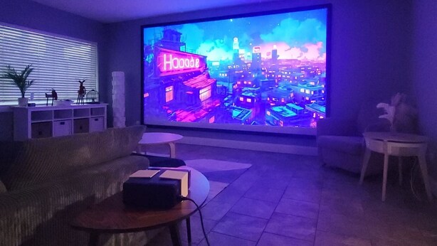 Een moderne woonkamer met een grote flatscreen-tv waarop een stadsbeeld te zien is. Er is een bank, een salontafel en een bijzettafeltje.