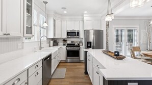 A modern kitchen with white cabinetry, stainless steel appliances, and pendant lighting. - Seabrook Along for the Ride | Hot Tub, Dog Friendly, Carriage House, Sleeps 14 (Pacific Beach)