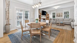 A modern living room with a dining area, a sofa, and a TV. - Seabrook Along for the Ride | Hot Tub, Dog Friendly, Carriage House, Sleeps 14 (Pacific Beach)