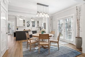 A modern kitchen with white cabinetry, a central island, and a dining area with a round table and chairs.