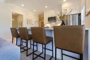 A modern kitchen with white cabinetry, a stainless steel refrigerator, a microwave, and a vase with flowers on the island. - Seabrook's At Last, a loft in Town Center! (Pacific Beach)