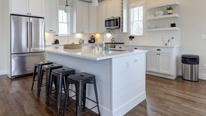 A modern kitchen with white cabinetry, stainless steel appliances, and a central island with stools. - Seabrook Aurum Hues | Ocean View, Hot Tub, Pet Friendly, 4BR, Sleeps 10 (Pacific Beach)