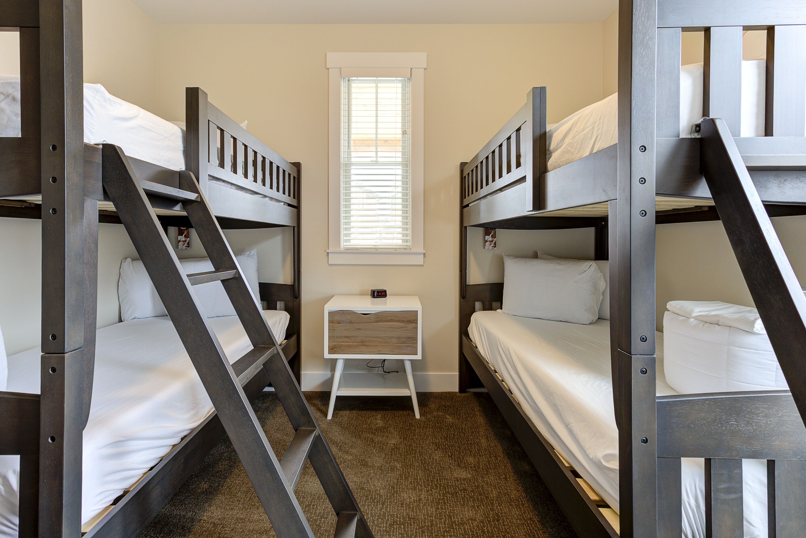 A room with bunk beds, a small bedside table, and a window.