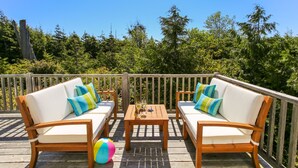 A wooden deck with two white cushioned sofas, each with colorful striped pillows, and a small wooden table with drinks. - Seabrook's Beachcomber: Dog Friendly! (Pacific Beach)