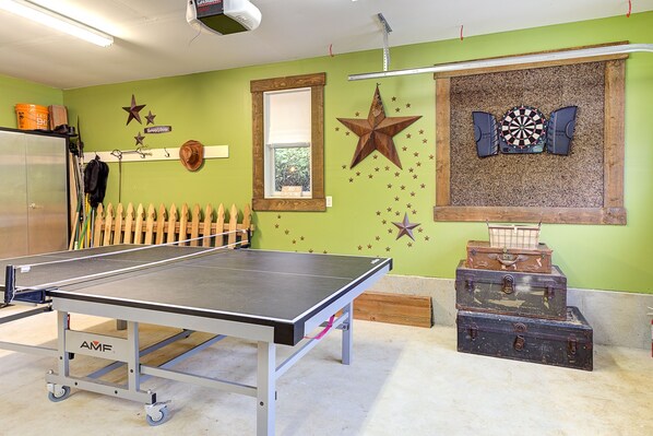 Una mesa de ping pong en una habitación con paredes verdes, un dardo y varias maletas.