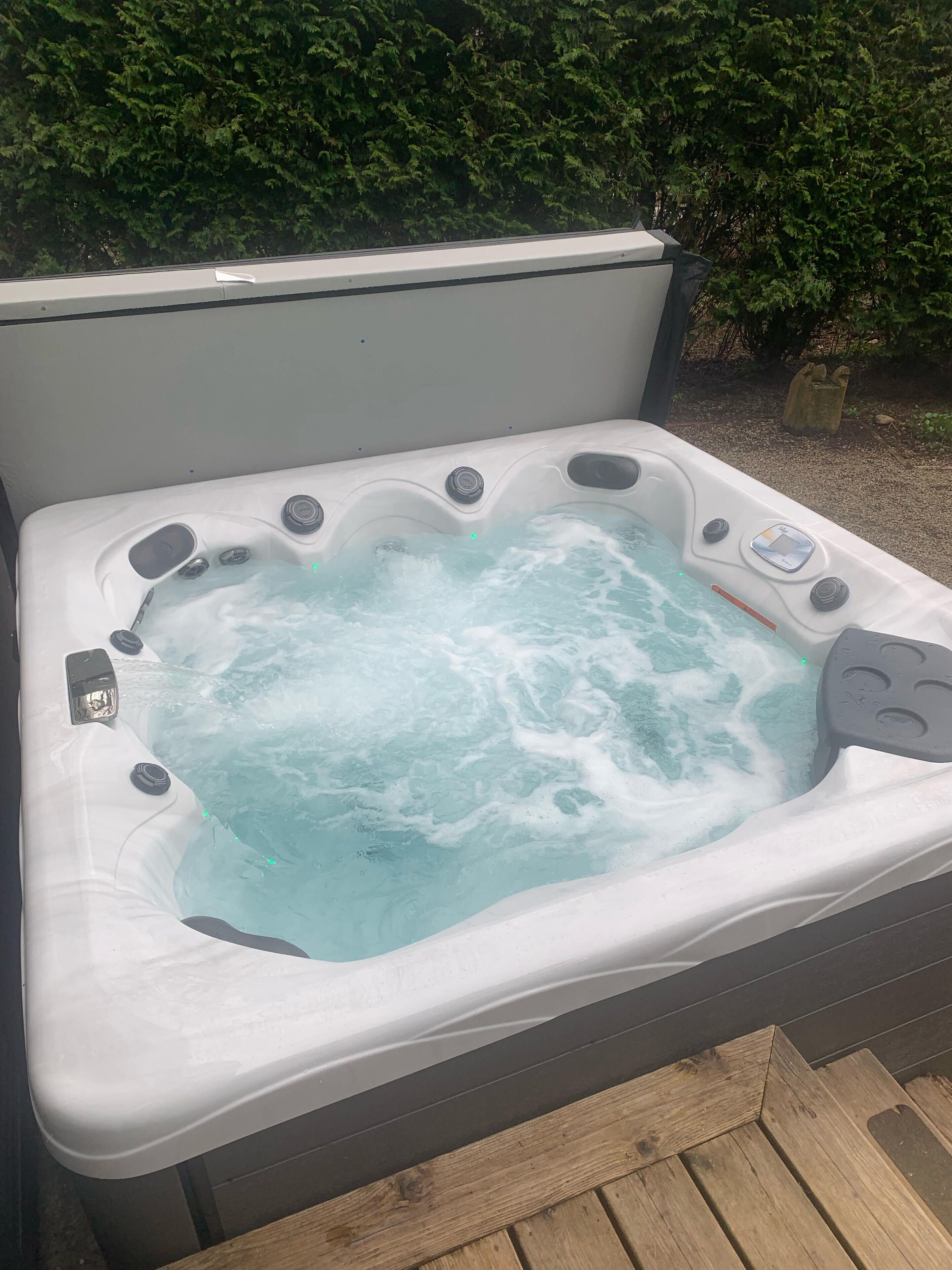 A hot tub with multiple jets, surrounded by a wooden deck and greenery.