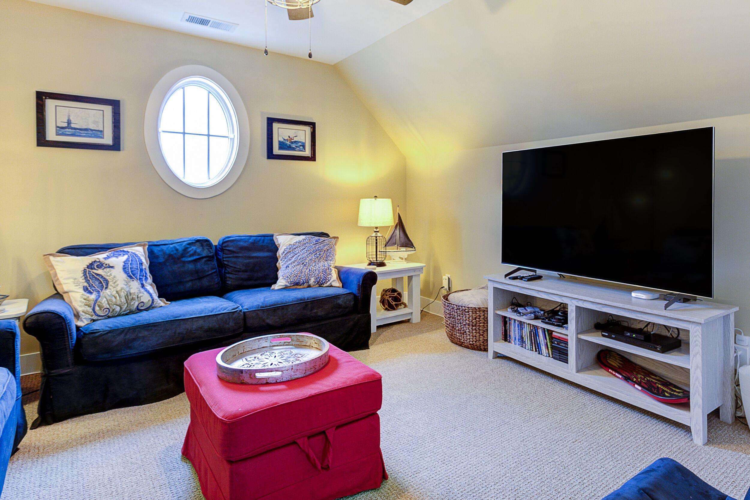 Een woonkamer met een blauwe bank, een rode poef, een televisie en een boekenkast.