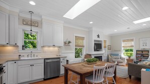 A modern kitchen with white cabinetry, a wooden dining table, and a cozy living area with a fireplace. - Seabrook's Beachy Keen, a private hot tub (Pacific Beach)