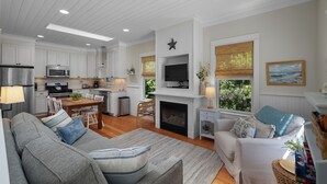 A modern living room with a fireplace, a television mounted above it, and a dining area with a table and chairs. - Seabrook's Beachy Keen, a private hot tub (Pacific Beach)