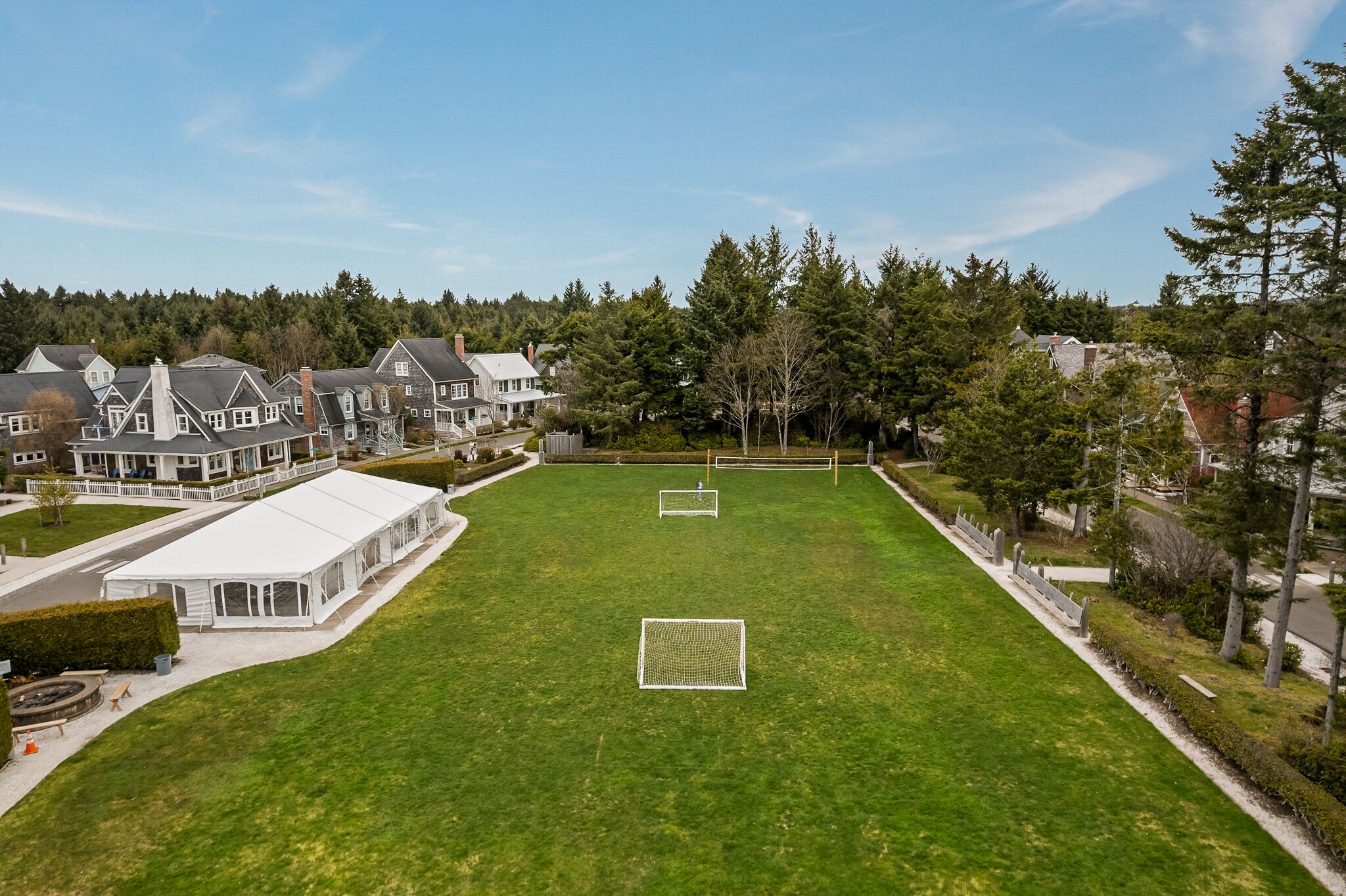 A large, well-maintained grassy field with two soccer goals, surrounded by residential houses and trees.