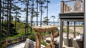 A wooden deck with outdoor furniture, overlooking a beach and forested area.