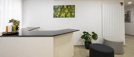 A reception area with a black reception desk, a potted plant, and a grey ottoman.