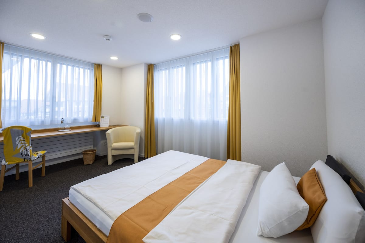 A hotel room with a bed, a desk, a chair, and a window with curtains.