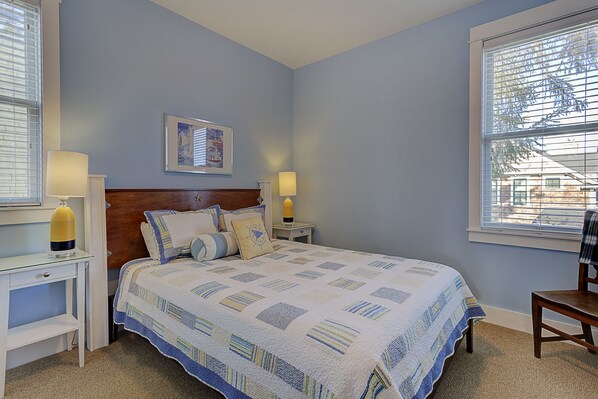 A bedroom with a large bed, two bedside tables with lamps, a headboard, a framed picture on the wall, and a window with blinds. - Seabrook Boat House | Hot Tub, Pool, Family | 3BR, Sleeps 8, Crescent Park (Pacific Beach)