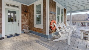 Een overdekt terras met houten gevel, een bord met de tekst 'Boat House', witte buitenstoelen en een reddingsboei.