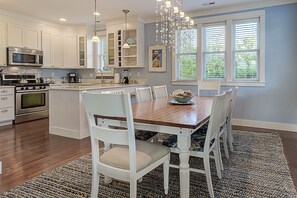 A modern kitchen with white cabinetry, a wooden dining table, and a chandelier. - Seabrook's Boat House,  a spacious home steps away from the indoor pool! (Pacific Beach)
