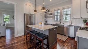 Une cuisine moderne dotée d’un îlot central, d’appareils électroménagers en acier inoxydable et de tabourets de bar en bois.