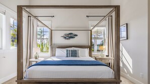 Un lit à baldaquin avec une couvre-lit blanche et bleue, une tête de lit en bois et un banc capitonné placé devant.