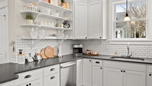 Une cuisine moderne avec des meubles blancs, un plan de travail noir et une fenêtre donnant sur une maison.