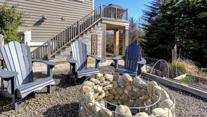Una terraza con sillas Adirondack, un hogar de piedra y una escalera que lleva a un porche cubierto.