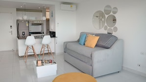 En moderne stue med en grå sofa, to hvide stole, et sofabord og et spejl monteret på væggen.