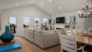 Ein geräumiges Wohnzimmer mit einem großen, beigefarbenen Ecksofa, einem Holzesstzimmer mit weißen Stühlen und einer Kristallleuchter.
