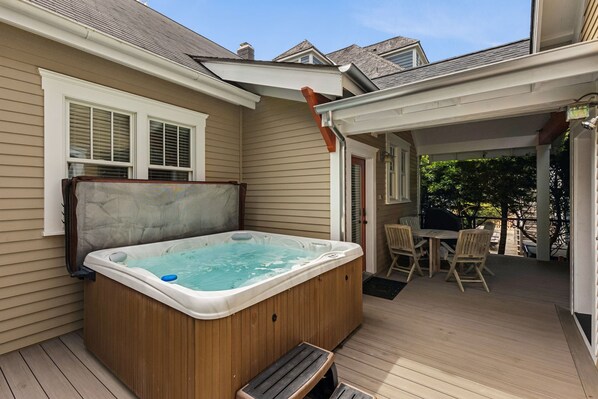 A hot tub on a wooden deck with a covered patio area and a table with chairs.