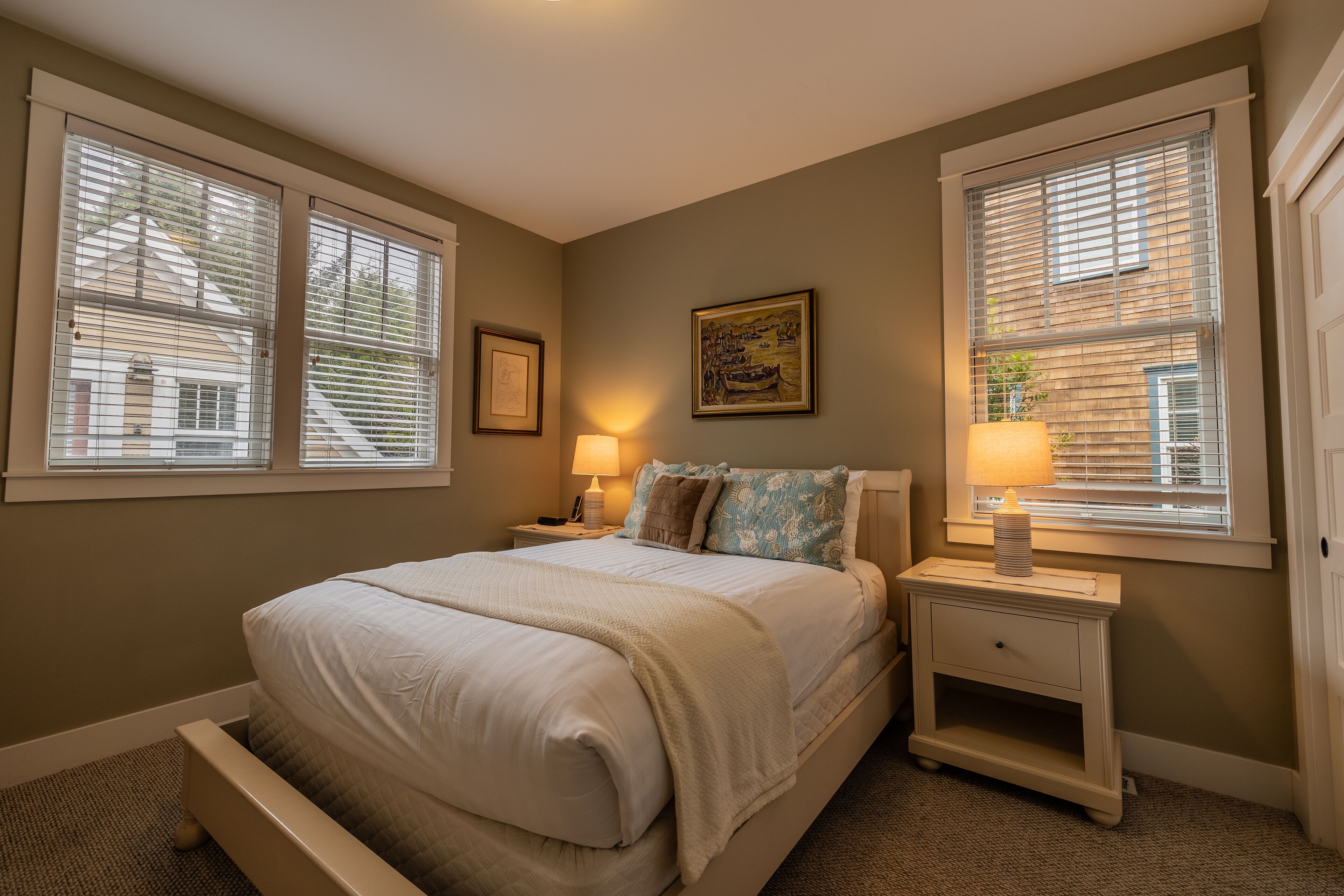 A bedroom with a bed, nightstands, a lamp, and a window with blinds.