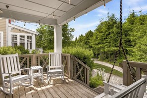 A wooden deck with Adirondack chairs, a hanging swing, and a view of a forested area. - Seabrook Creekside Cottage | Hot Tub, Location 3BR | Sleeps 6, South Farm (Pacific Beach)