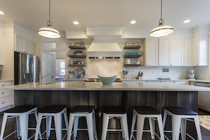 Een moderne keuken met witte kastjes, een groot eiland met barkrukken en hanglampen.