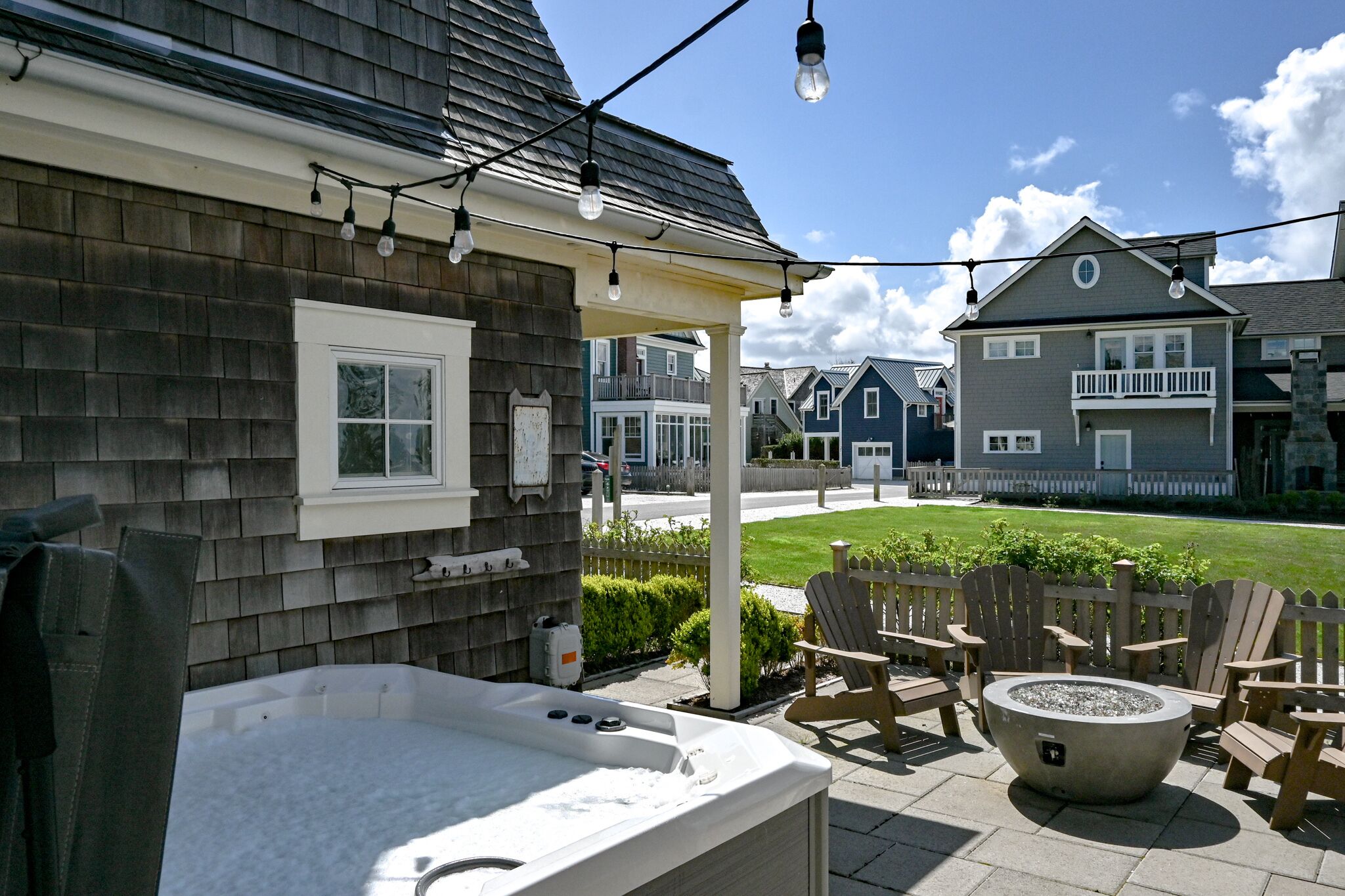 A backyard with a hot tub, outdoor seating, and string lights.