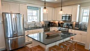 A modern kitchen with white cabinetry, stainless steel appliances, a central island with stools, and pendant lighting. - Seabrook Eagles Nest | Ocean View, Hot Tub | 5BR, Sleeps 14, West Hill Park (Pacific Beach)