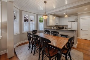 A dining area with a wooden table and chairs, white cabinets, and a hanging light fixture.