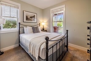 A bedroom with a bed, two bedside tables, a lamp, and a window with blinds.