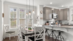 A kitchen with white cabinetry, a central island with stools, a dining table with chairs, and pendant lighting.
