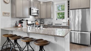 A modern kitchen with a central island, stainless steel appliances, and bar stools.