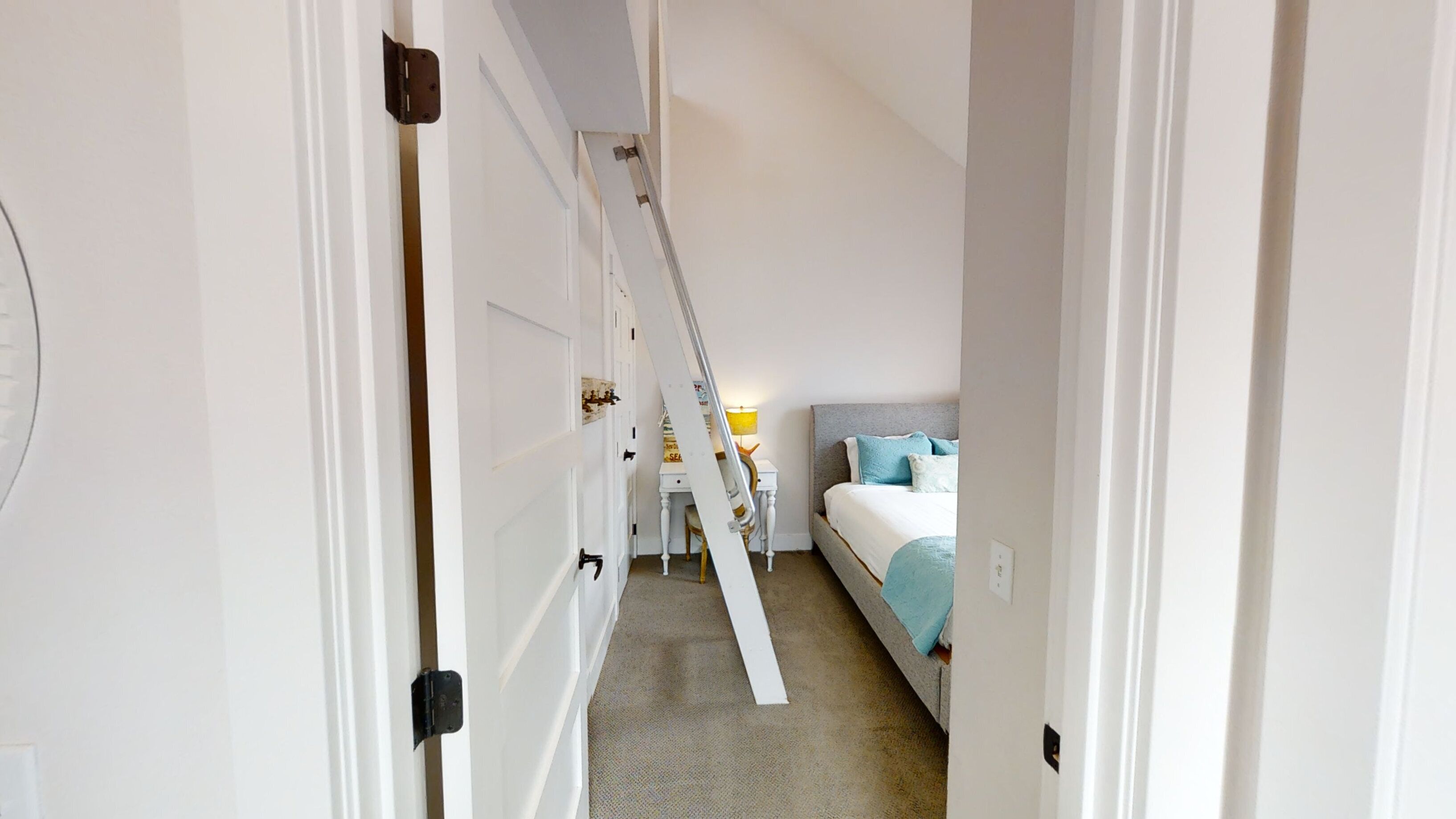 A narrow hallway leading to a bedroom with a bed, a nightstand, and a lamp.