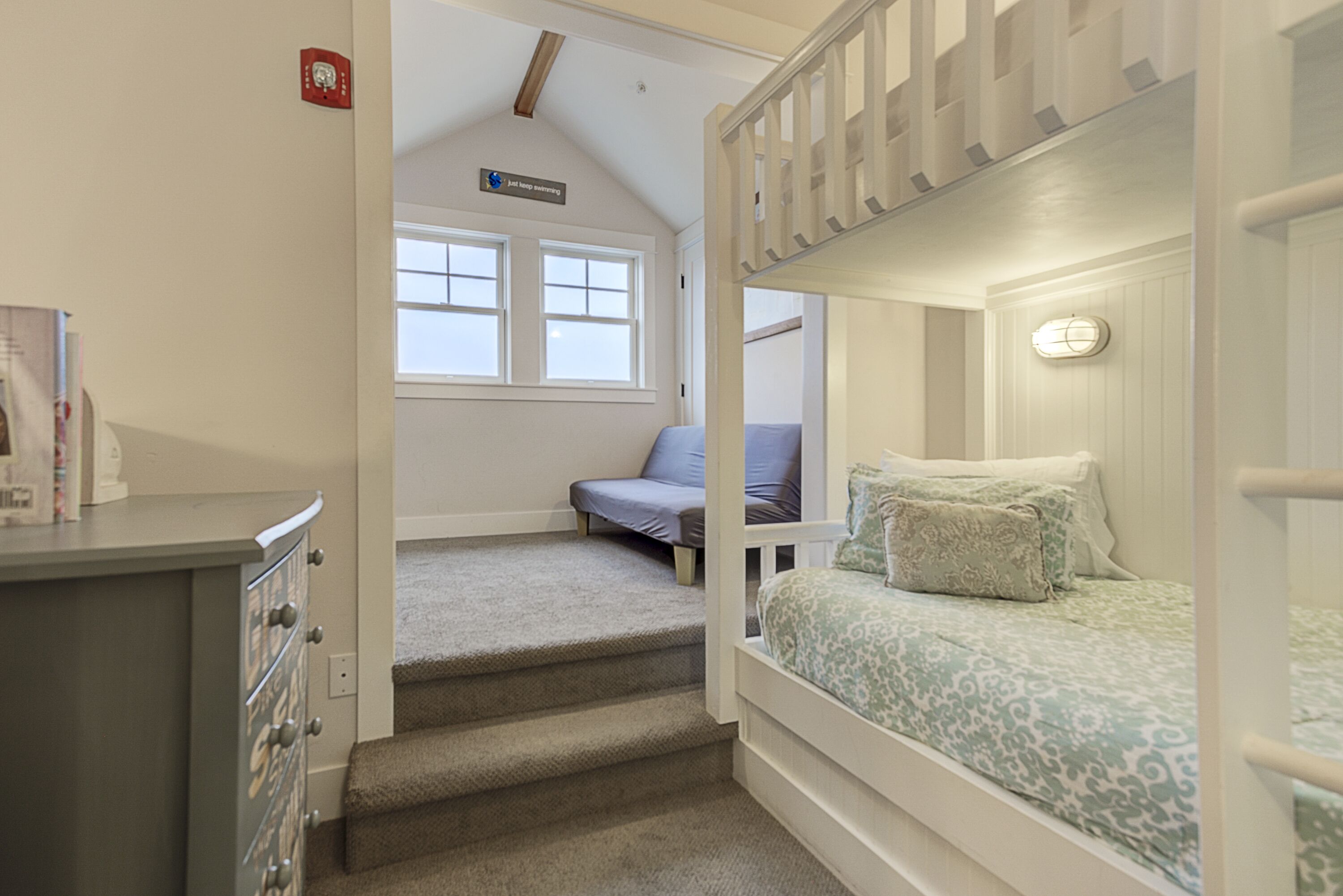 A bedroom with bunk beds, a desk, and a chair. There are stairs leading to a loft area with a window.