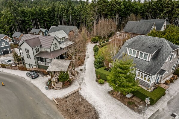 A residential area with multiple houses, a gravel driveway, and a forested background. - Seabrook Flotsam House | Hot Tub, Family, 2BR | Sleeps 6, Mill District (Pacific Beach)