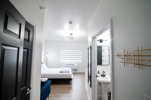 A narrow hallway leading to a bedroom with a bed, a window with blinds, a ceiling fan, and a wall-mounted mirror. - Conestoga Quarters (Jefferson City)