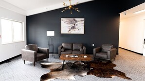 A modern living room with a dark wall, a chandelier, a coffee table, leather chairs, and a large fur rug. - Conestoga Quarters (Jefferson City)
