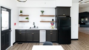 A modern kitchen with dark cabinetry, a black refrigerator, and wooden shelves with plants. - Conestoga Quarters (Jefferson City)