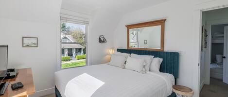 A bedroom with a large bed, a wooden desk, a mirror, and a view of the outside.