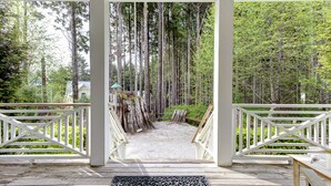 A wooden deck with a white railing, leading to a gravel path surrounded by tall trees. - Seabrook Dog-Friendly Cottage | Hot Tub & Indoor Pool | Family Stay (Pacific Beach)