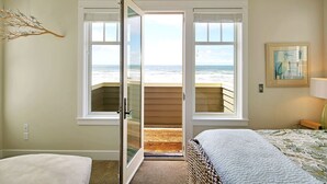 Ein Schlafzimmer mit großem Fenster mit Blick auf einen Strand, einem Bett und einem Gemälde an der Wand.
