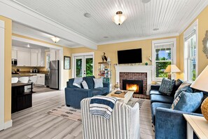 A spacious living room with a fireplace, a kitchen with white cabinets, and a dining area with a table and chairs.