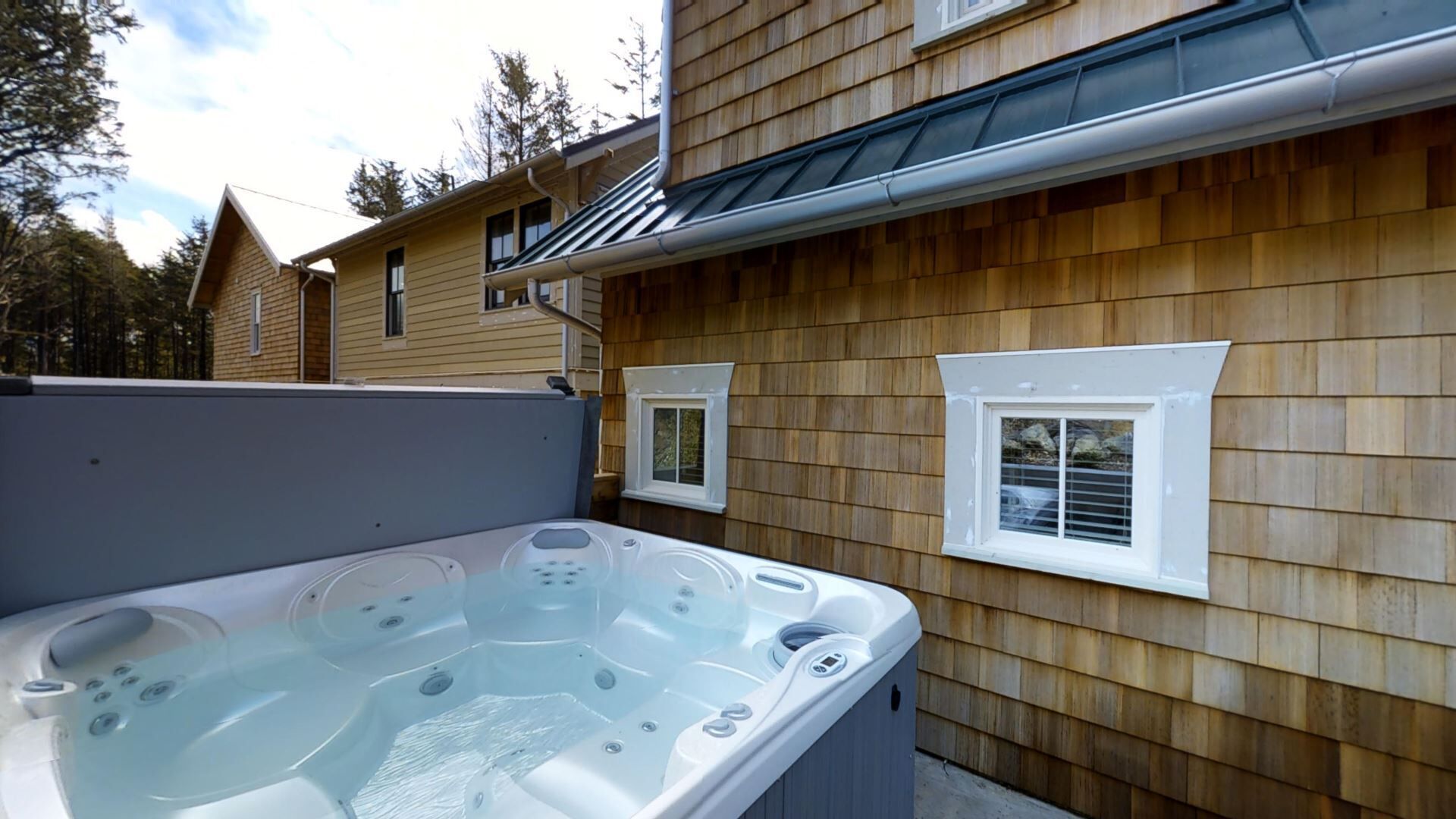Un bain à remous situé à côté d’une maison en bois dotée de deux fenêtres.