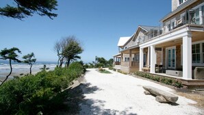 Una proprietà fronte spiaggia con veranda coperta, un vialetto sabbioso e vista sull'oceano.
